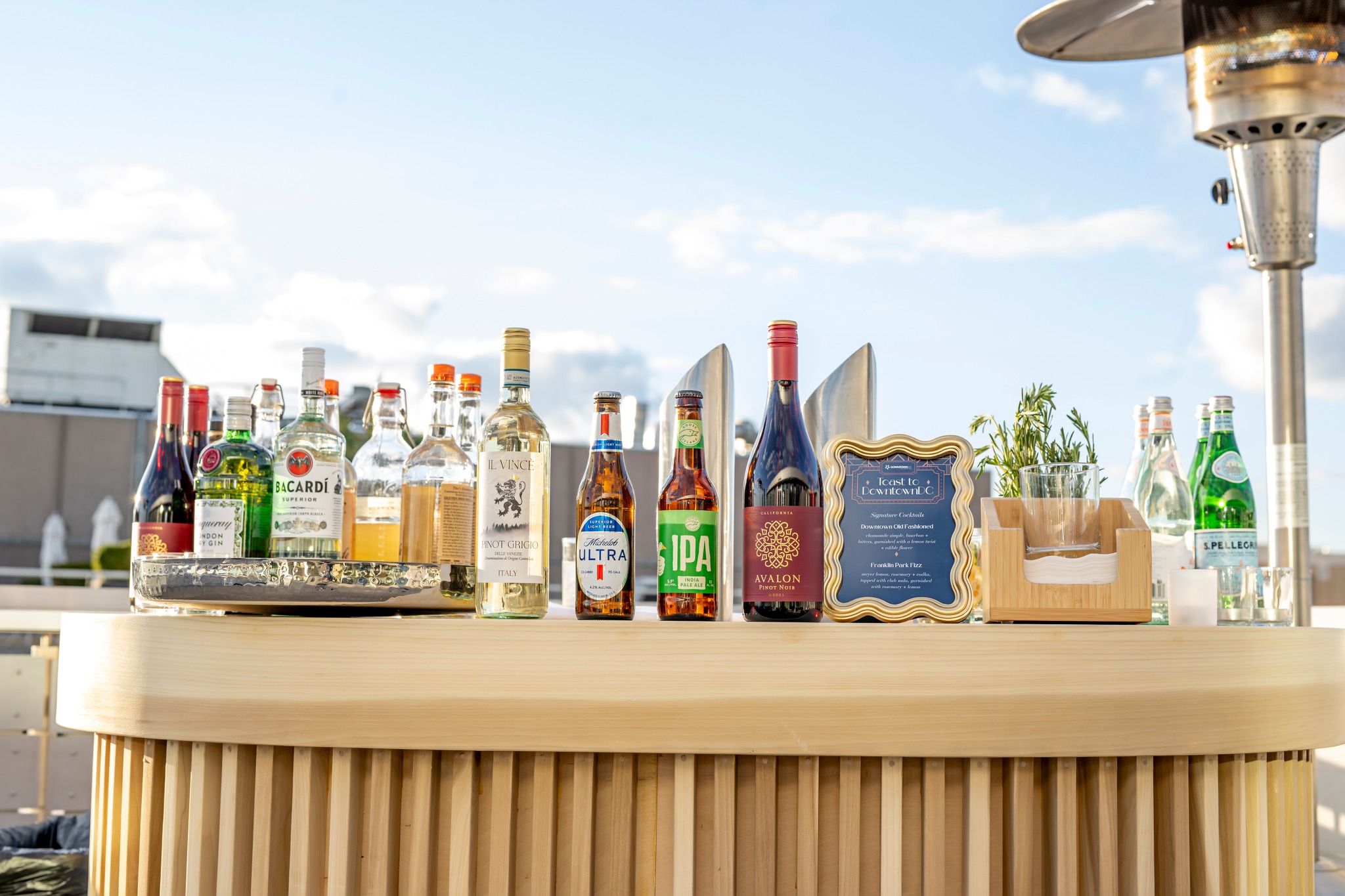 A row of bottles of alcohol on a bar top with a view of the city in the background